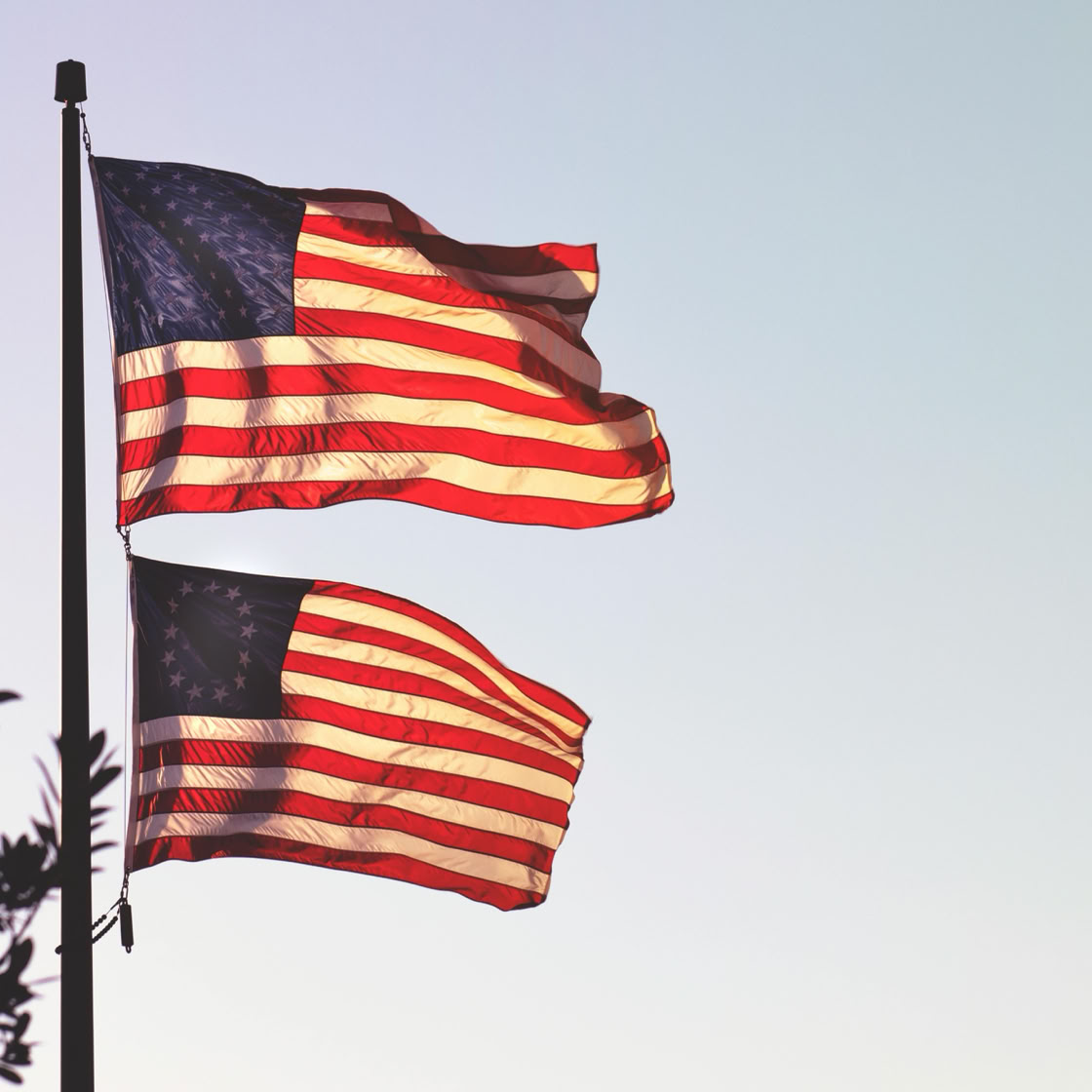 Two American flags waving on a pole during a calm morning sunrise in Atascadero, California.